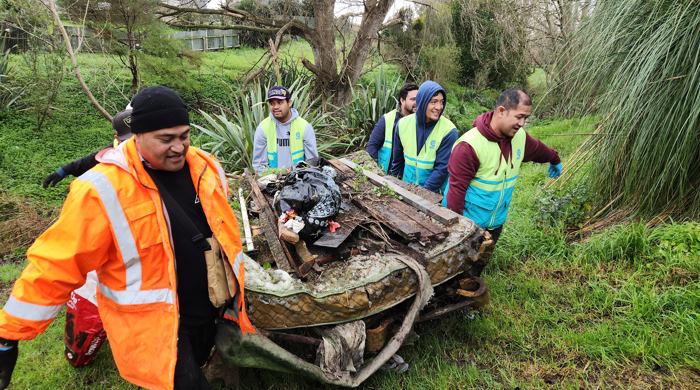People working together to haul an old mattress and bed base, wood and other rubbish from an urban stream.