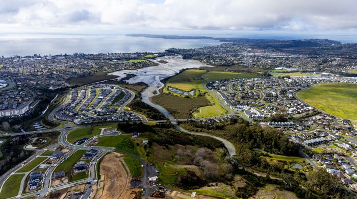 An aerial view of a river and estuary surrounded by housing with more land being cleared back to clay in the foreground.